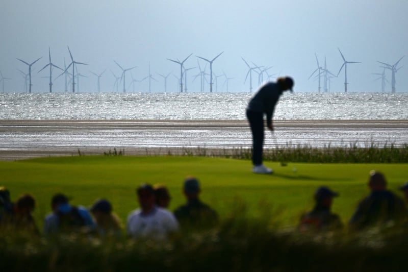 Wind turbines at the Burbo Bank Offshore windfarm are pictured on the horizon as England’s Tommy Fleetwood putts on the 13th green.