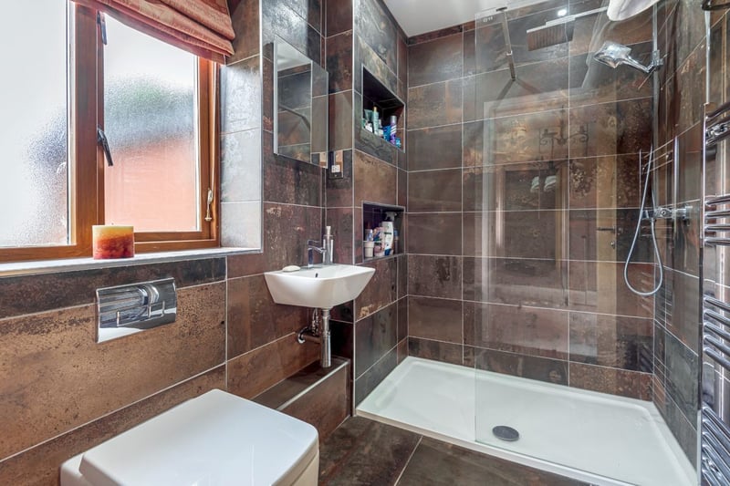 The contemporary ensuite has a white suite comprising an enclosed WC, a handwash basin with a mixer tap, a walk-in shower with a waterfall shower. (Photo - Zoopla)