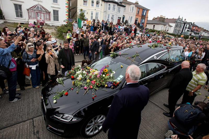 People lay flowers and tributes on the hearse during the funeral procession of late Irish singer Sinead O'Connor, outside the former home in Bray, eastern Ireland, ahead of her funeral on August 8, 2023. A funeral service for Sinead O'Connor, the outspoken singer who rose to international fame in the 1990s, is to be held on Tuesday in the Irish seaside town of Bray. (Photo by PAUL FAITH/AFP via Getty Images)