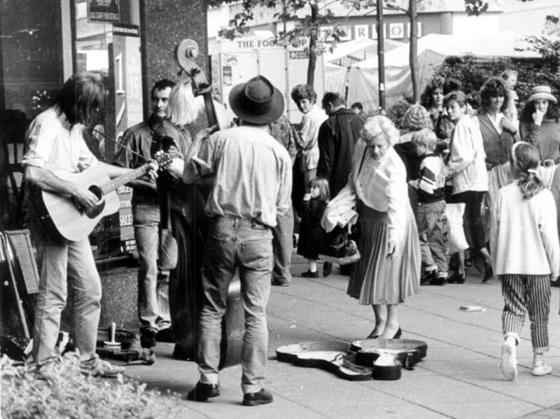 A woman stops to throw some money into a guitar case as buskers entertain shoppers on The Moor in Sheffield city centre in 1990. Photo: Picture Sheffield