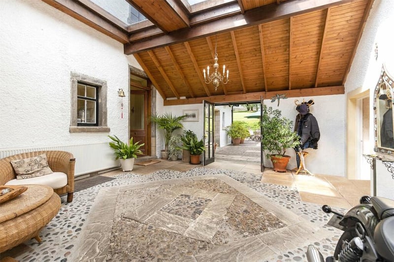 Entrance to the property is through an architect-designed covered courtyard created by bridging between the main house and the out-houses. This space is filled with mature planting and has a high vaulted ceiling, raised skylights, feature stone flooring and internal heating. 