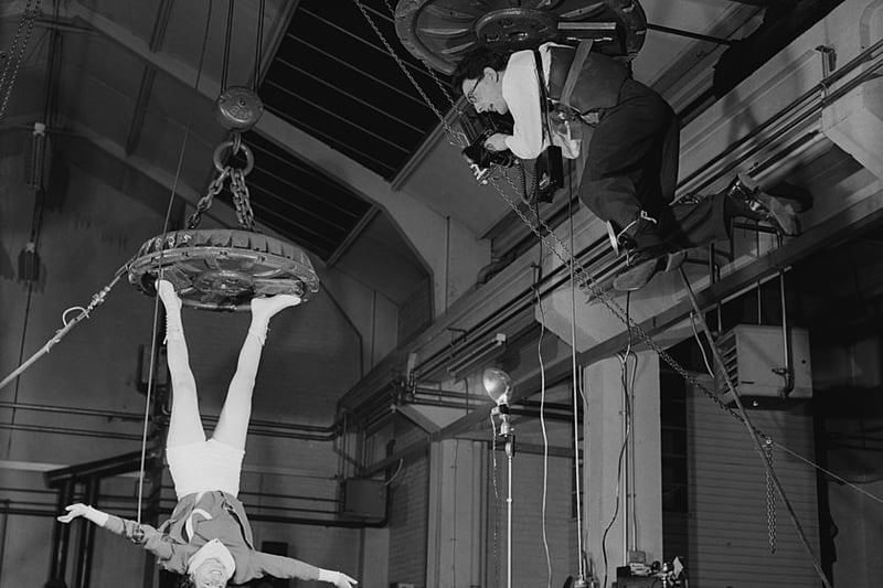 Fox Photos photographer Derek Berwin is hoisted up on an electromagnet at the Boxmag works in Birmingham, in order to take a photograph of typist Kathleen Reddington who is similarly suspended, December 1957. Kathleen is hanging from a 40 inch magnet by her ice skates. (Photo by Fox Photos/Hulton Archive/Getty Images)