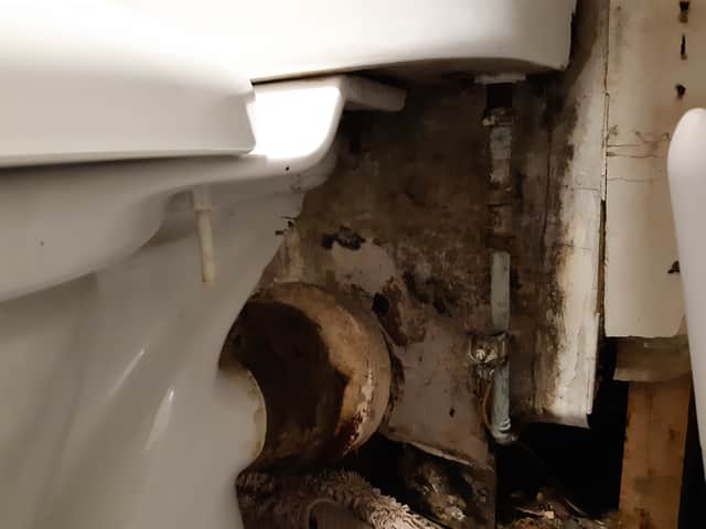 Black mould behind the toilet, which has been 'secured' with adhesive tape.