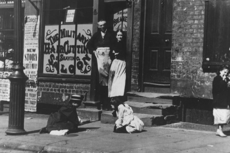 Children play ‘Jacks and Allies’ outside a barber’s shop with its striped pole.