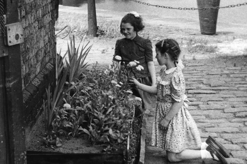 Two young girls placing flowers in a small dockland garden on the banks of the River Mersey.