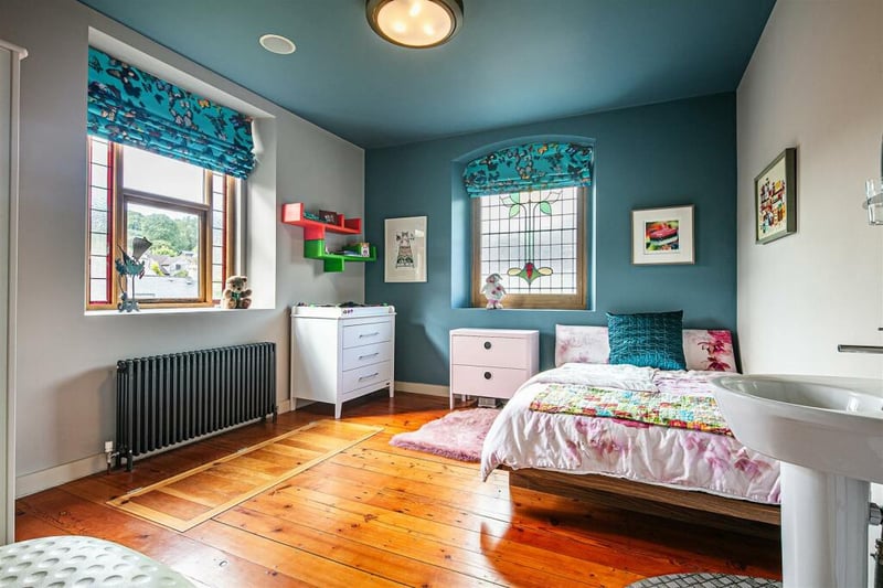 This second first-floor bedroom is the smallest of the three but still spacious, including a sink, stained glass window, and wooden floors.