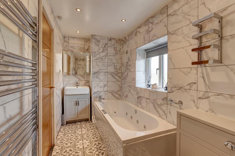 The main bathroom has a double glazed obscured window, recessed lighting, chrome heated towel rail and an illuminated vanity cabinet. It includes a panelled spa bath, walk-in shower enclosure with a fitted rain head shower.