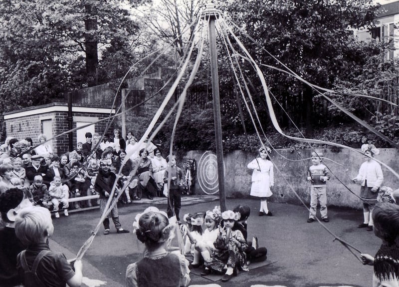 Children of Hucklow First School, Firth Park, Sheffield, dancing round the maypole before an audience of parents in the schoolyard, in May 1983