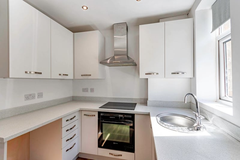 The kitchen includes an electric oven and gas hob with extractor above, and a circular stainless steel sink with mixer tap set beneath the rear window. 