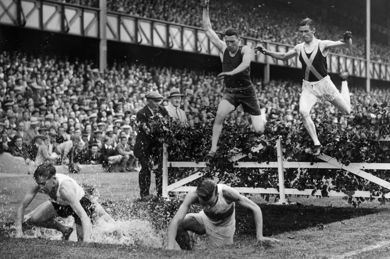 Competitors leaping over the water jump in an eight lap steeplechase event during the 49th annual sports day of the Rangers Football Club held at Ibrox Park stadium. Features of the main stand are still present till this day. 