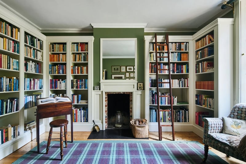 The spectacular library with muted green walls and an open fire place 