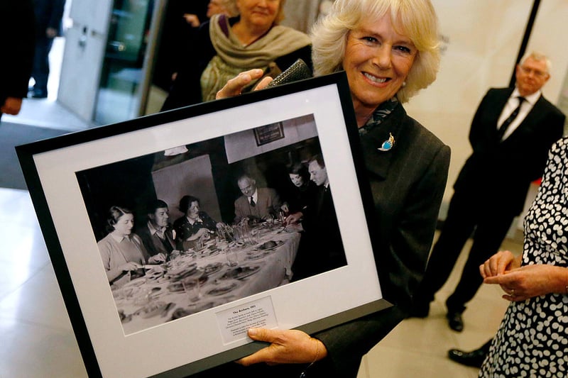 Queen Camilla poses with a picture of the original “Archers” radio soap cast given to her during a visit to the British Broadcasting Corporation (BBC) at New Broadcasting House on February 11, 2014 in London.  (Photo by Luke MacGregor - WPA Pool/Getty Images)