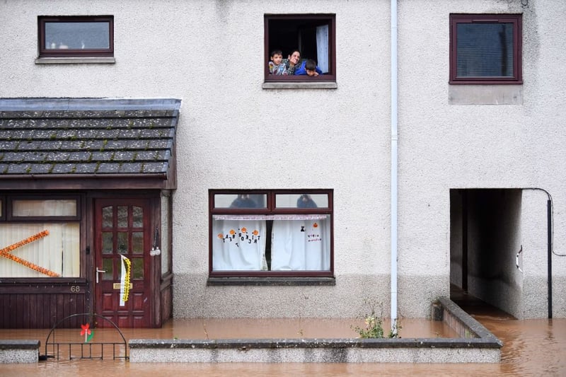 A family trapped in the upper floor of their home look out a window in a flooded Brechin street.