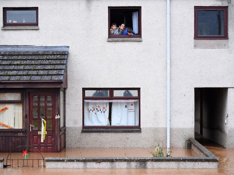 A family trapped in the upper floor of their home look out a window in a flooded Brechin street.