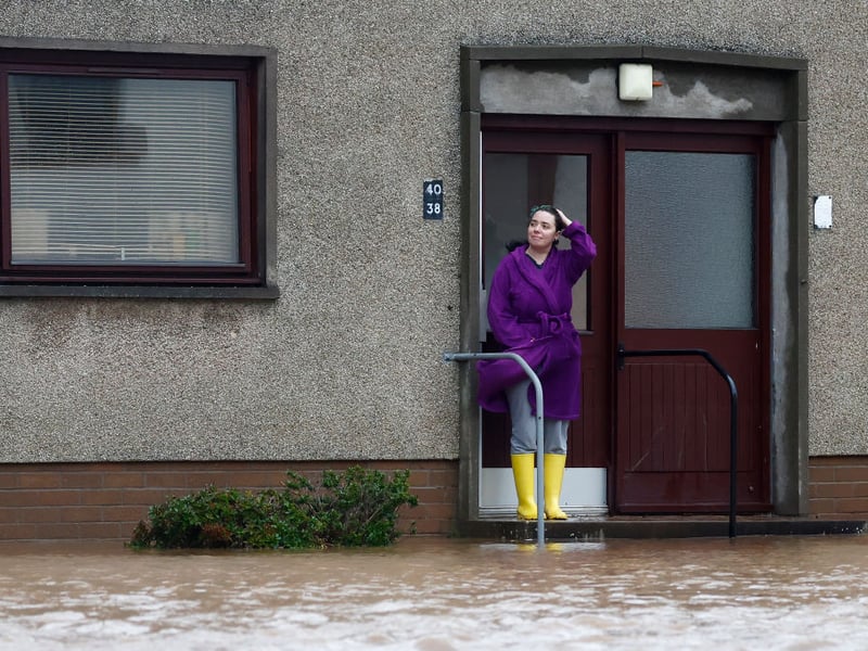 A woman surveys the flooding and waits for help on the doorstep of her Brechin home.