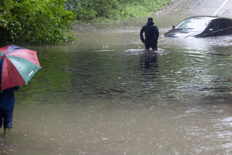 A man wades into the water to inspect a stranded car and ensure no one is trapped 