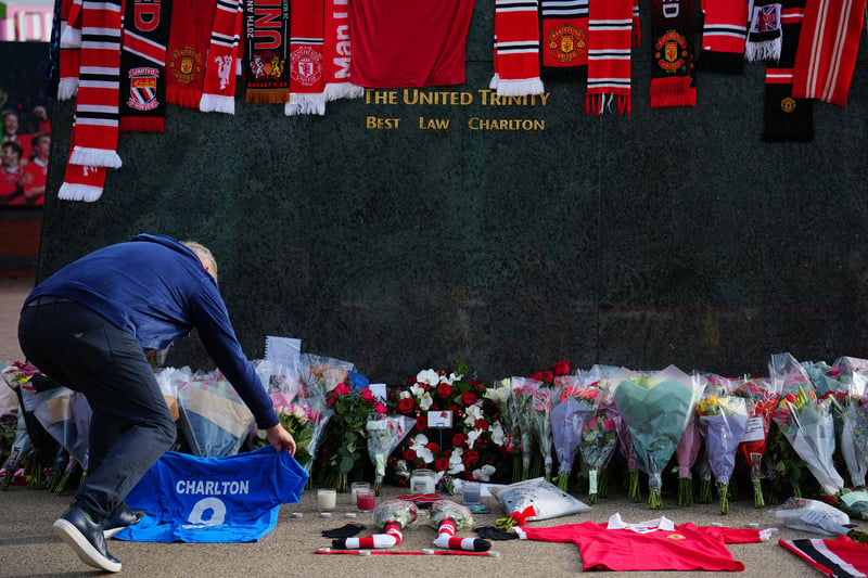 A fan lays a football shirt in tribute at the base of the 'United Trinity' sculpture, depicting former Manchester United players George Best, Denis Law and Bobby Charlton, following the death of Bobby Charlton, outside of Old Trafford