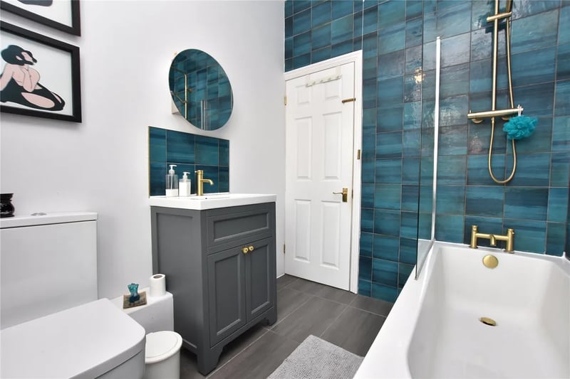 The house bathroom with bathtub and shower over with blue tiling.