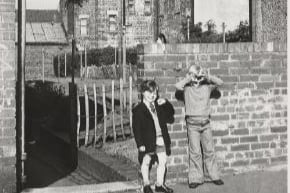 Two small boys stand in front of a brick wall with tenement buildings behind - taken from Church Street.