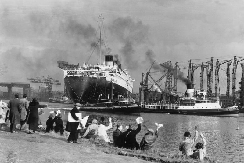 Crowds gather to watch the new Cunard White Star liner Queen Mary leaving her fitting-out berth in the John Brown & Co shipyard at Clydebank. Handkerchiefs are waved as the massive liner makes her way down the river Clyde to the sea, en route to Greenock and Southampton.