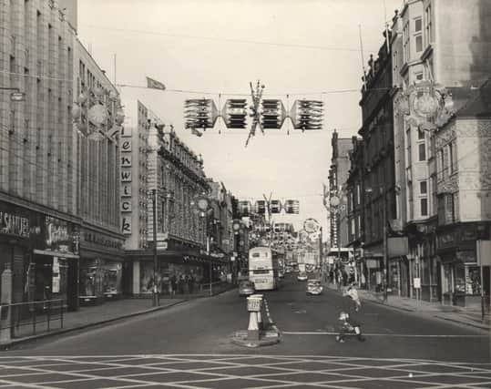 A view of Northumberland Street Newcastle upon Tyne taken in 1966. The photograph shows the Christmas decorations on Northumberland Street. The shops on the left-hand side of Northumberland Street include ‘H. Samuel’ ‘F. W. Woolworths’ and ‘Fenwick’s’. The shops on the right-hand side include ‘Amos Atkinson’ and ‘Littlewoods’. (Newcastle Libraries)