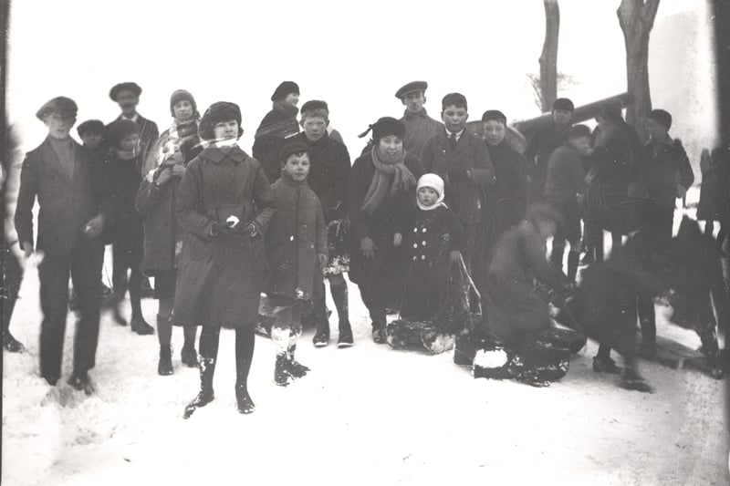A photograph of children playing in the snow taken c.1930. Some of the children have wooden sledges. Adults can be seen in the background. (Newcastle Libraries)