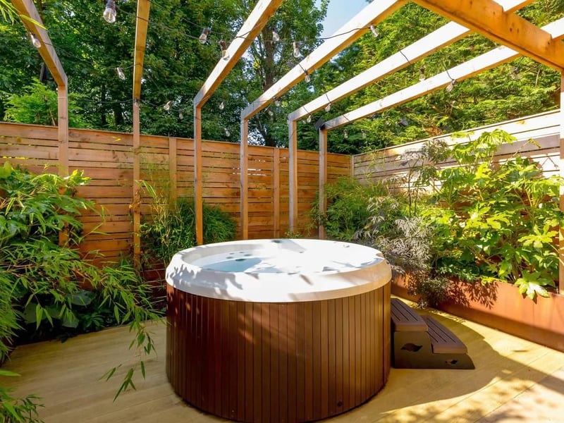 A luxurious hot tub is part of a large outdoor living area that includes outdoor seating, a dining area under a wisteria and climbing rose-trellised oak pergola.