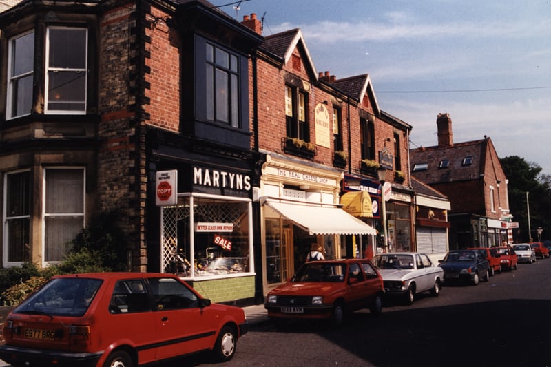  A view of Acorn Road Jesmond taken in 1996. The photograph shows a row of shops on the left-hand side of Acorn Road. The shops include ‘Martyns’ shoe shop ‘The Real Cheese Shop’ and ‘Browns Gallery’. A row of cars are parked in front of the shops (Newcastle Libraries).