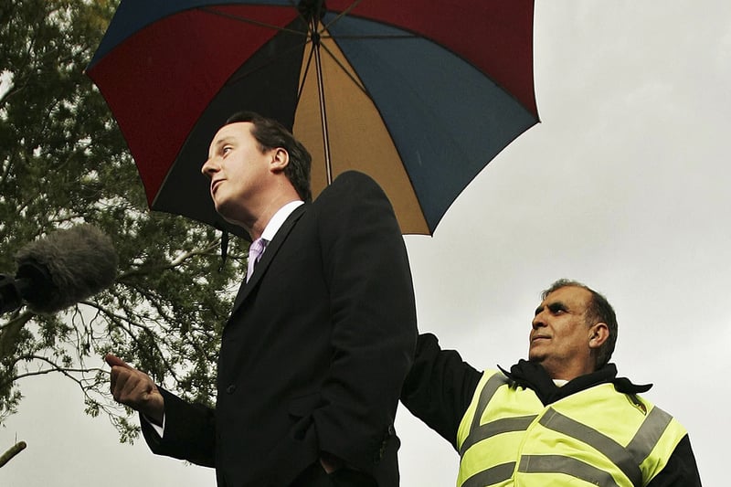 A local man holds an umbrella as Conservative Party Leadership challenger David Cameron gives a media interview whilst campaigning in Balsall Heath on October 23, 2005 to become Conservative Party leader