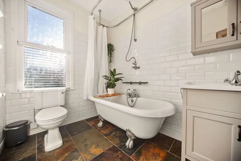 The bathroom has stunning tiled floor and a roll-top bathtub.