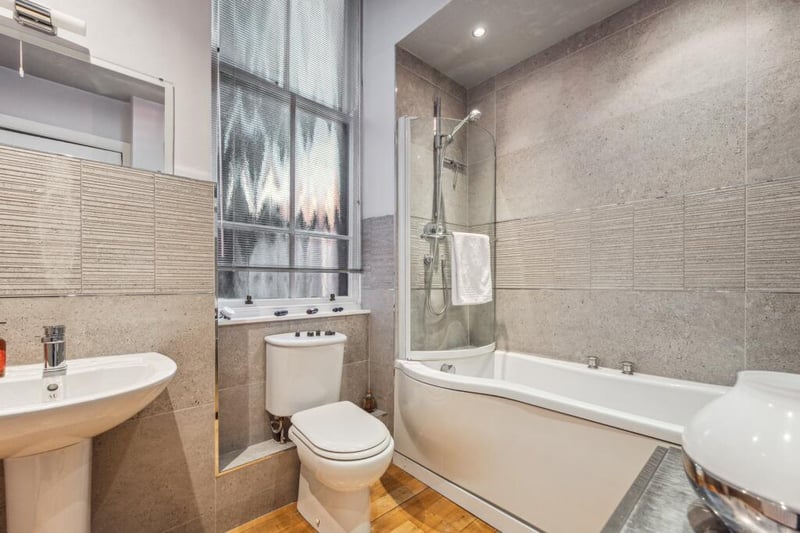 The main white bathroom suite features Porcelanosa tiles and a shower above the bath. 