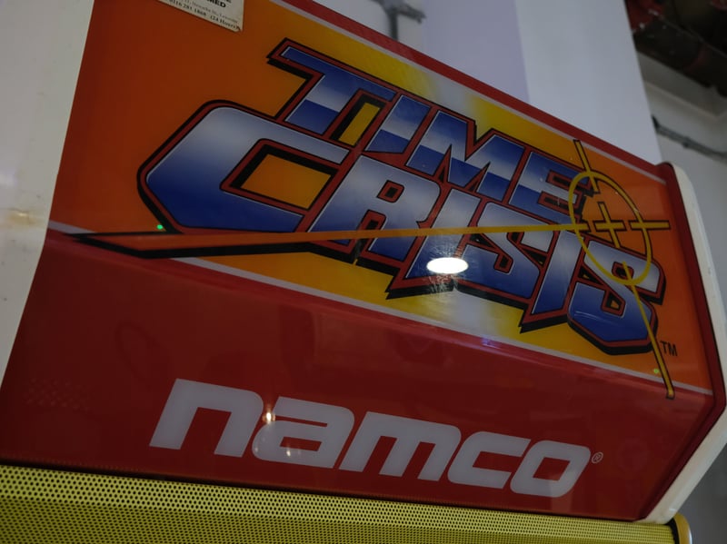 Time Crisis is a first-person on-rails light gun shooter series of arcade video games by Namco, introduced in 1995. Alex Hughes, crew/shift leader at the NVM, said: "A beautifully crafted slice of old school rail shooting. The inherently restrictive and simple nature of the rail shooter format means the game is free to go off like a rocket with a sense of action movie spectacle you usually wouldn't see this side of Just Cause or Platinum games titles. Within minutes of starting the game you're blowing up cars, blasting ninjas and fighting your way to the climactic showdown with a man who genuinely thinks that "Wild Dog" is a cool name. The incredibly tactile gun controller that physically recoils with every shot combined with the story of a lone gunman out to rescue the president's daughter against overwhelming odds lead to a wonderful game feel that remains unmatched. Light gun games and rail shooters are basically non-existent in today's gaming climate so absolutely give this one a go!”