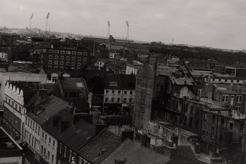 The photograph has been taken from the John Dobson Street flats looking west. There are shops on Saville Row in the foreground to the left. Shops on Northumberland Street can be seen in the centre. The floodlights of St. James Park can be seen in the background.