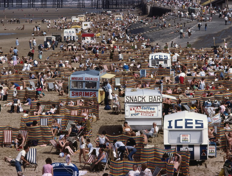 Crowds of holidaymakers and kiosks offering tea, coffee, ices, whelks and cockles and shrimps as snacks on the beach in 1983
