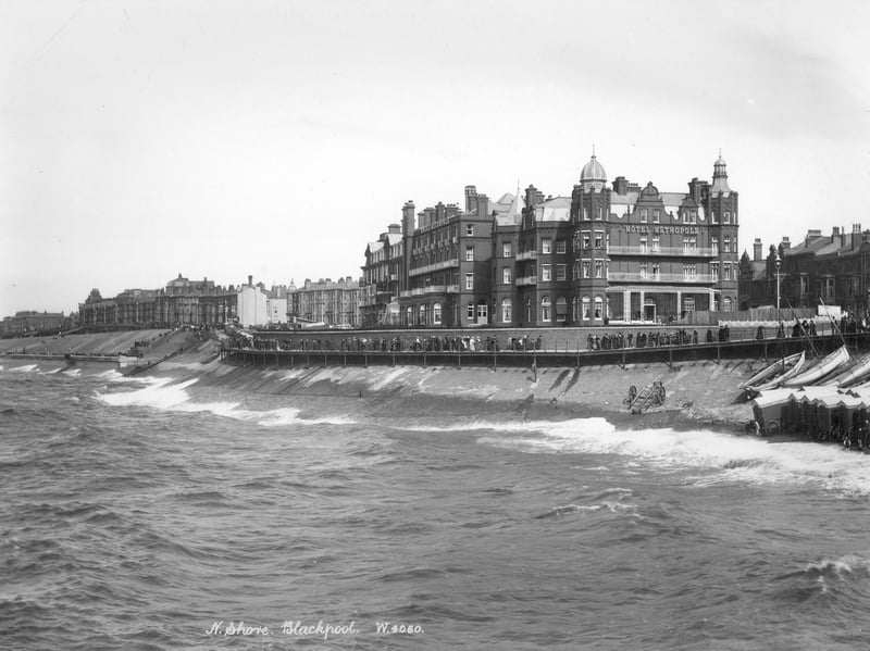 The Metropole Hotel, 1890-1910. The north shore with people walking along the promenade by the Victorian Hotel Metropole. Beach huts have been pulled closer to the railings out of the way of the rough sea