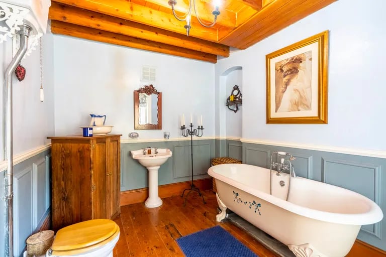 The house bathroom is a gorgeous suite with wooden floors, a roll-top bathtub and exposed original beams.