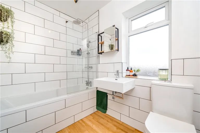 The tiled bathroom has a bathtub with shower over.