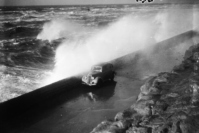 3rd December 1936:  A huge wave breaks over the sea wall and showers a passing car on the seafront at Blackpool.  (Photo by Fox Photos/Getty Images)