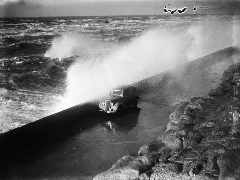 3rd December 1936: A huge wave breaks over the sea wall and showers a passing car on the seafront at Blackpool. (Photo by Fox Photos/Getty Images)