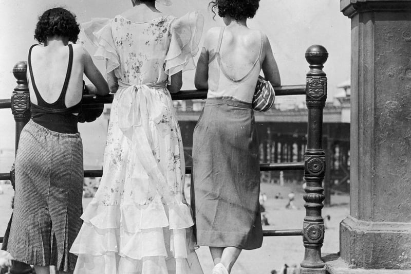Three women on Blackpool promenade during a heatwave. One wears a divided skirt and the other a straight skirt, both over swimwear. The middle one has a 'copy' of the Letty Lynton dress made popular by Joan Crawford in the film of that name. Adapted for the mass market the triple row of frills at the hem are matched by frills at the shoulder forming cap sleeves.   (Photo by E  Dean/Getty Images)