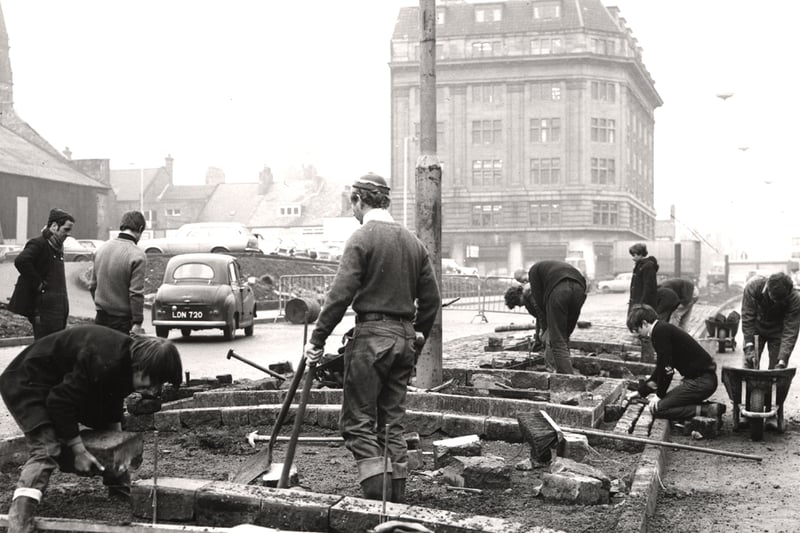  A view of John Dobson Street/Northumberland Road Newcastle upon Tyne taken in 1969. In the foreground men are laying paving stones on the island which divides the two lanes on John Dobson Street. Buildings on Northumberland Road can be seen in the background with the tower of St Thomas Church behind. 