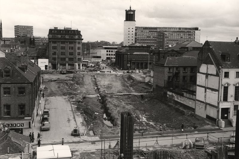 The photograph shows a section of John Dobson Street under construction. Saville row runs horizontally to the front of the picture. Just beyond the construction work is Northumberland Street the buildings on the right with pillars being the Northumberland Baths and to the right that the City Hall. 