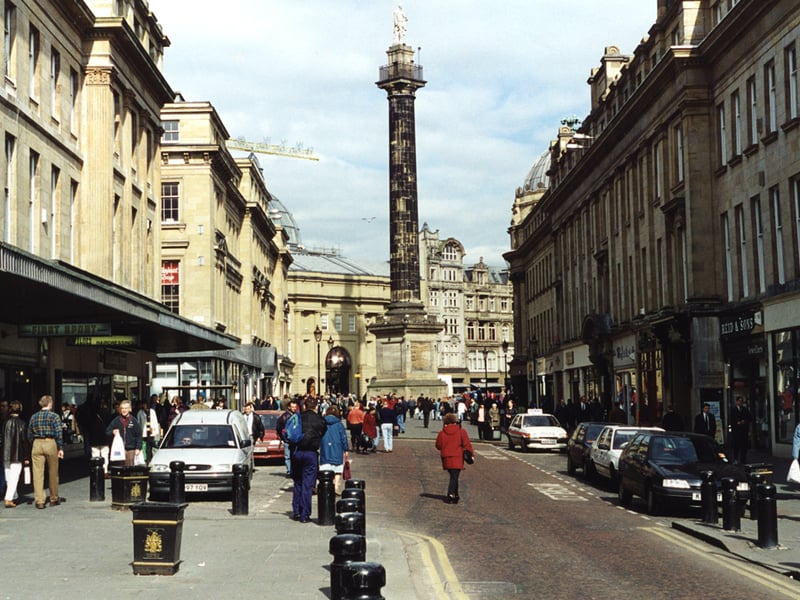 A view of Grainger Street Newcastle upon Tyne taken in 1995. The view is looking along Grainger Street towards Grey's Monument. It is a busy street scene. In the centre to the right is the entrance to the Central Arcade and to the left Nelson Street. Grey's Monument is in the background with Monument Mall behind. 