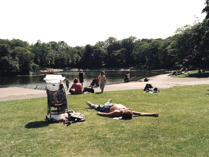 A view of Leazes Park Newcastle upon Tyne taken in 1996. The photograph shows people sunbathing beside the lake. A boat can be seen on the lake in the distance.