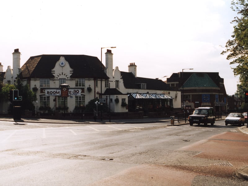 A 1995 photograph of the Corner House Hotel viewed from across Stephenson Road. The central section and right wing of the building can be seen. The People's Theatre is visible further down Stephenson Road. Cars are waiting at the traffic lights in the left hand lane of Stephenson Road.