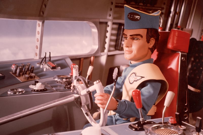 A marionette pilot in uniform steers a vehicle in a still from the television science fiction series, 'Thunderbirds,' circa 1965