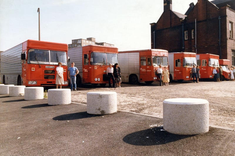 Leeds City Libraries' contingent of Mobile Libraries, parked in the yard outside the old library headquarters on York Road. The headquarters were based in the former York Road Branch Library and Public Baths building, seen on the right. Each mobile was staffed at the time by a driver and an assistant, seen pictured here outside their vans. The area in the foreground is now taken up by Great Clothes.