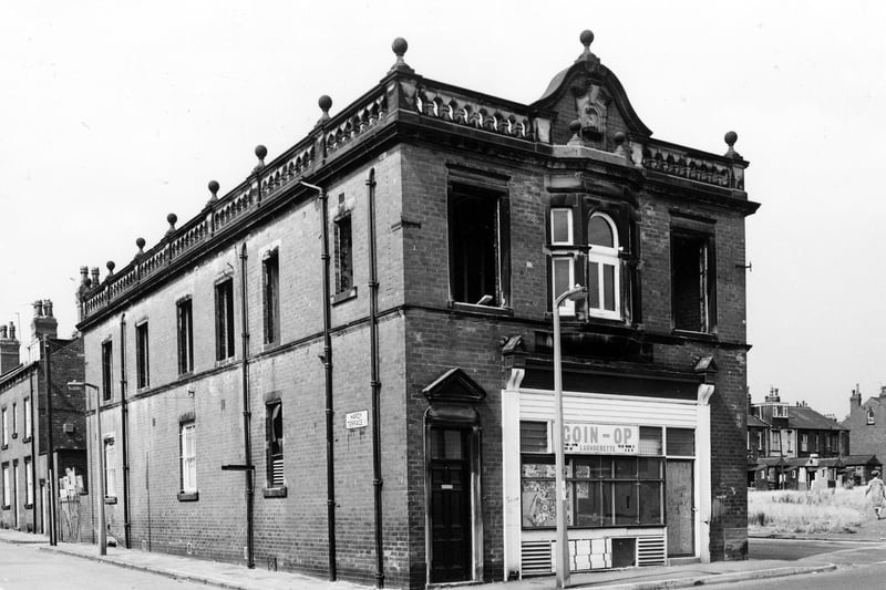 Lodge Lane showing the former Leeds Industrial Co-operative Building in Hardy Street at number 1. In the image it is undergoing conversion to the Kashmir Welfare Muslim Centre. Hardy Terrace is seen to the left of the building and Hardy Street is to the right. This side view of the premises shows a boarded up Coin-op Launderette. Waste ground at the right edge was once occupied by short streets of terraced homes - 'Ellis Place', 'Stewart Place' and 'Wood Place'. Tempest Place is visible behind, right. Pictured in July 1984.