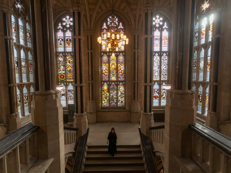 Communications officer, Jenny Francis, stands at the top of the grand staircase with the restored stained glass windows behind her. 