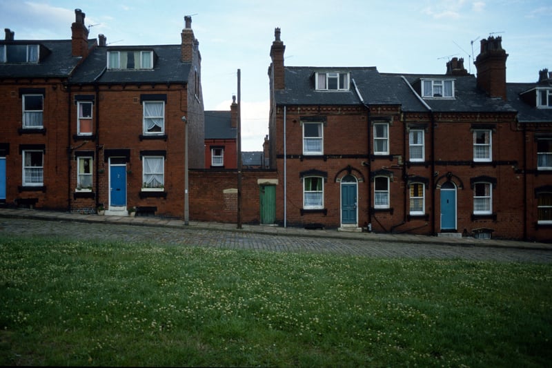 Red brick terraced housing on Thomas Street, seen from a cleared area where houses on the opposite side of Thomas Street (which were back-to-backs with Bolland Street) have been demolished. Houses on view are (from left) nos. 12 to 4. They form back-to-backs with Quarry Place, which is visible over the top of the shared toilet block in the centre. Pictured in August 1985.